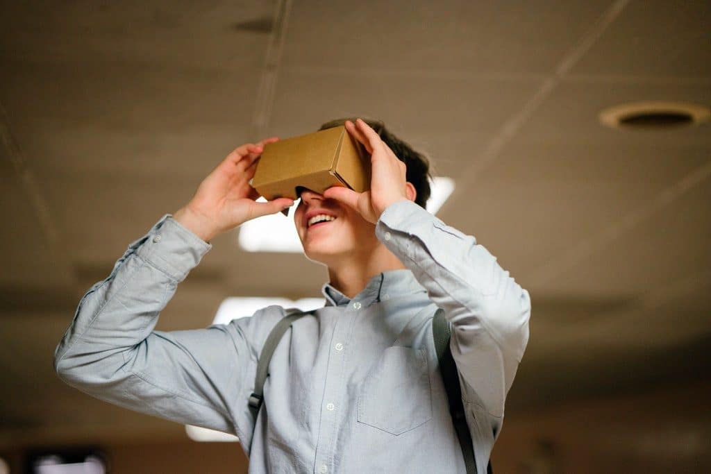 A young man in a button-down shirt holds a pair of cardboard goggles to his eyes.