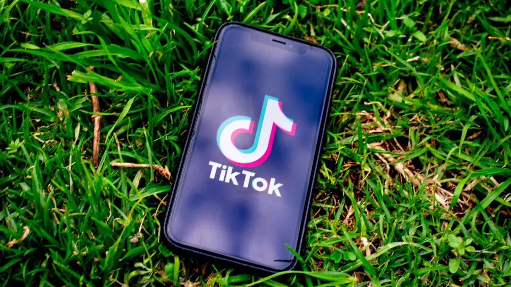 TikTok logo on iPhone on grass background - 5 Ways For Brands To Use TikTok For Growth